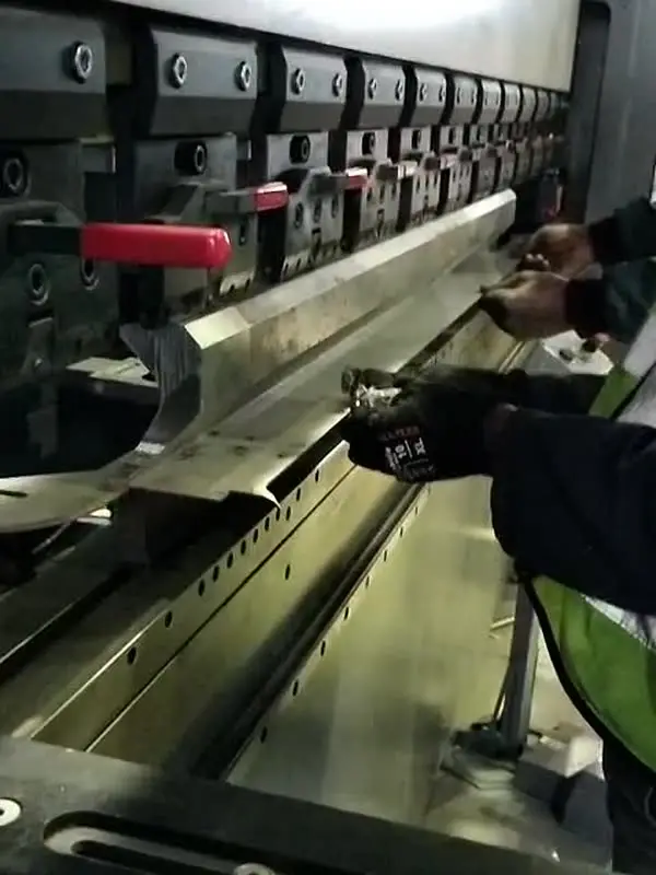 Gloved hands guiding a steel canopy part through the press brake